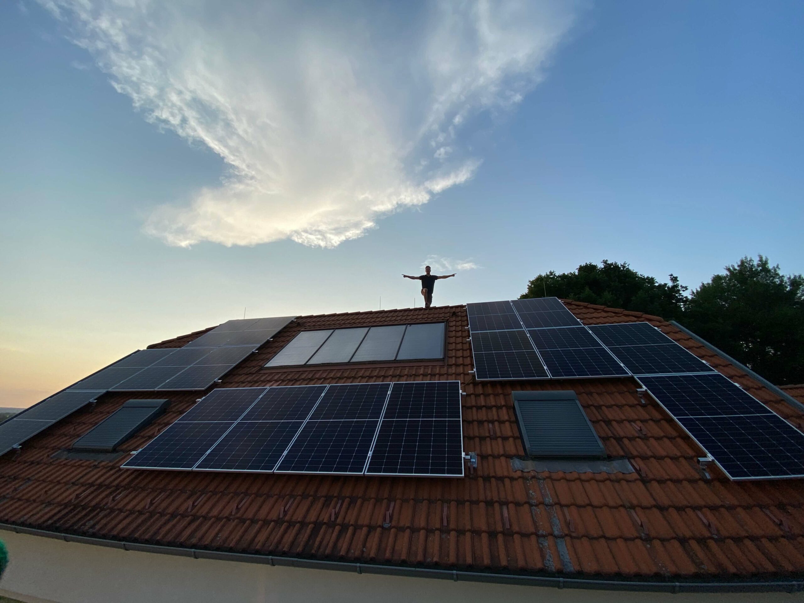 Photovoltaikanlage auf einem roten Dach und Person mit ausgetreckten Armen